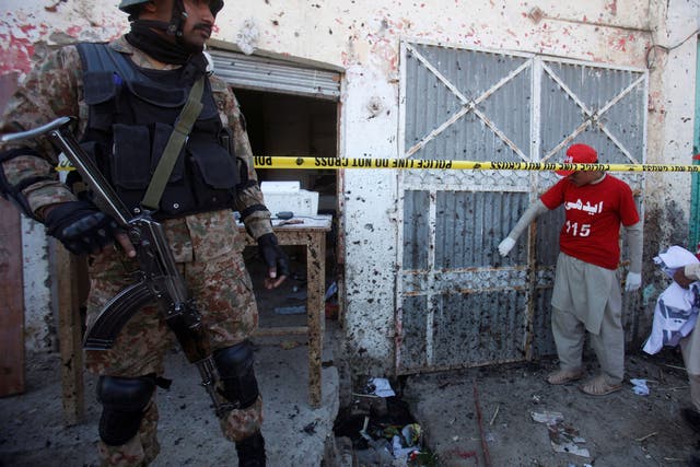 A soldier stands guard as voluteers collect remains of the walls and doors around the site of a blast at the courthouse in Charsadda, Pakistan, 21 February