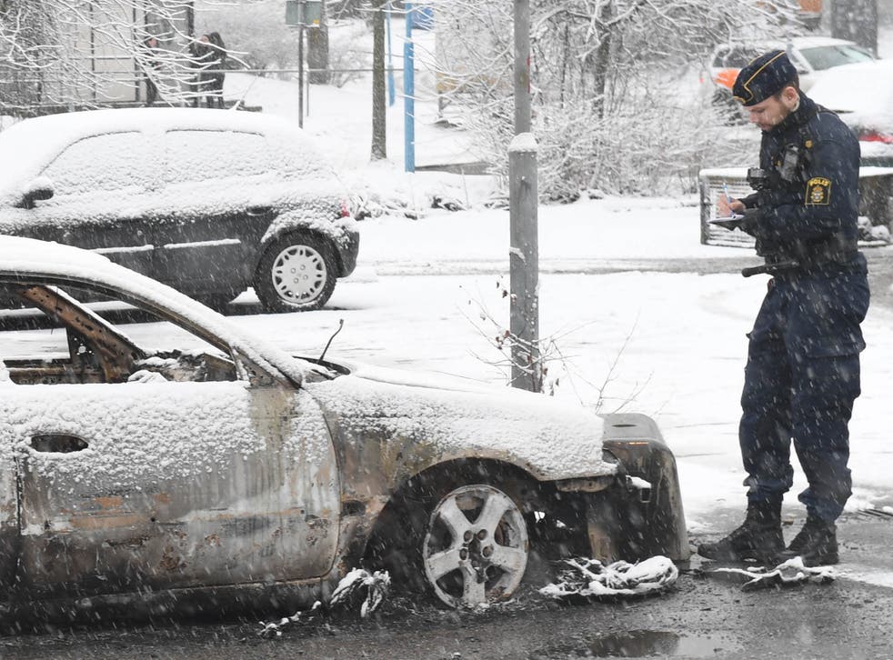 A police officer investigates a burned-out car in the suburb of Rinkeby outside Stockholm