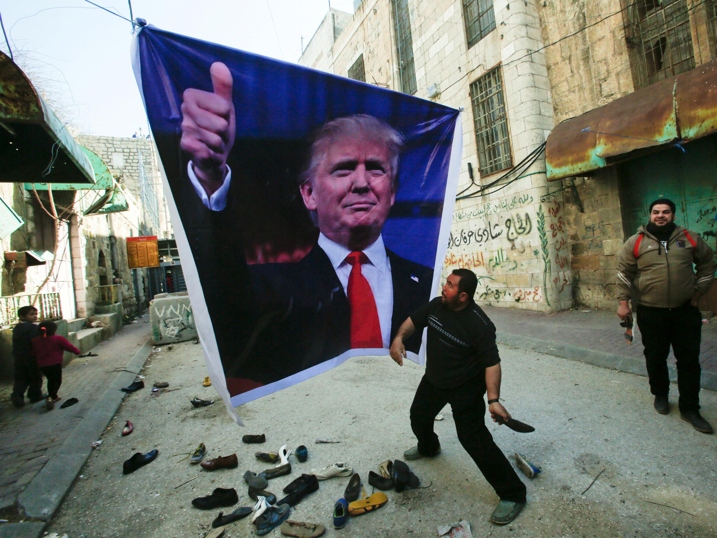 A Palestinian demonstrator throws a shoe at a poster of US President Donald Trump during a protest in the West Bank city of Hebron