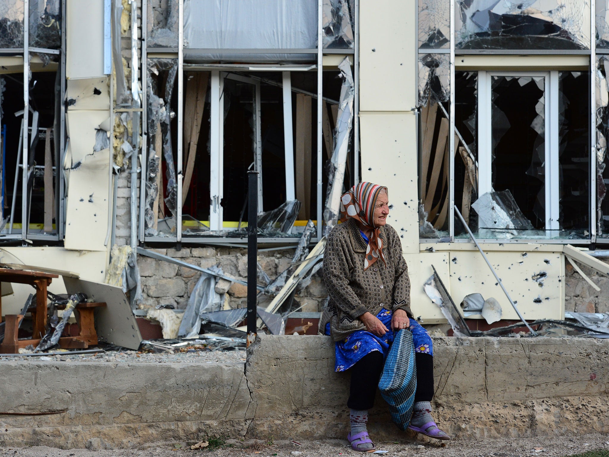 An elderly woman sits outside a damaged building in Pervomaisk, which is held by rebels loyal to the Lugansk People's Republic