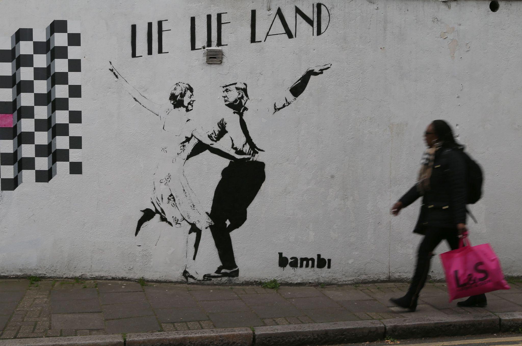 A woman walks past a mural by English street artist Bambi depicting British Prime Minister Theresa May dancing with US President Donald Trump in London on February 22, 2017