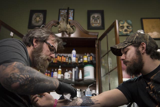 Tattoo parlor owner Dave Cutlip, left, creates an eagle design to cover a tattoo of a Confederate flag on the arm of Randy Stiles, 25, in Brooklyn Park, Maryland