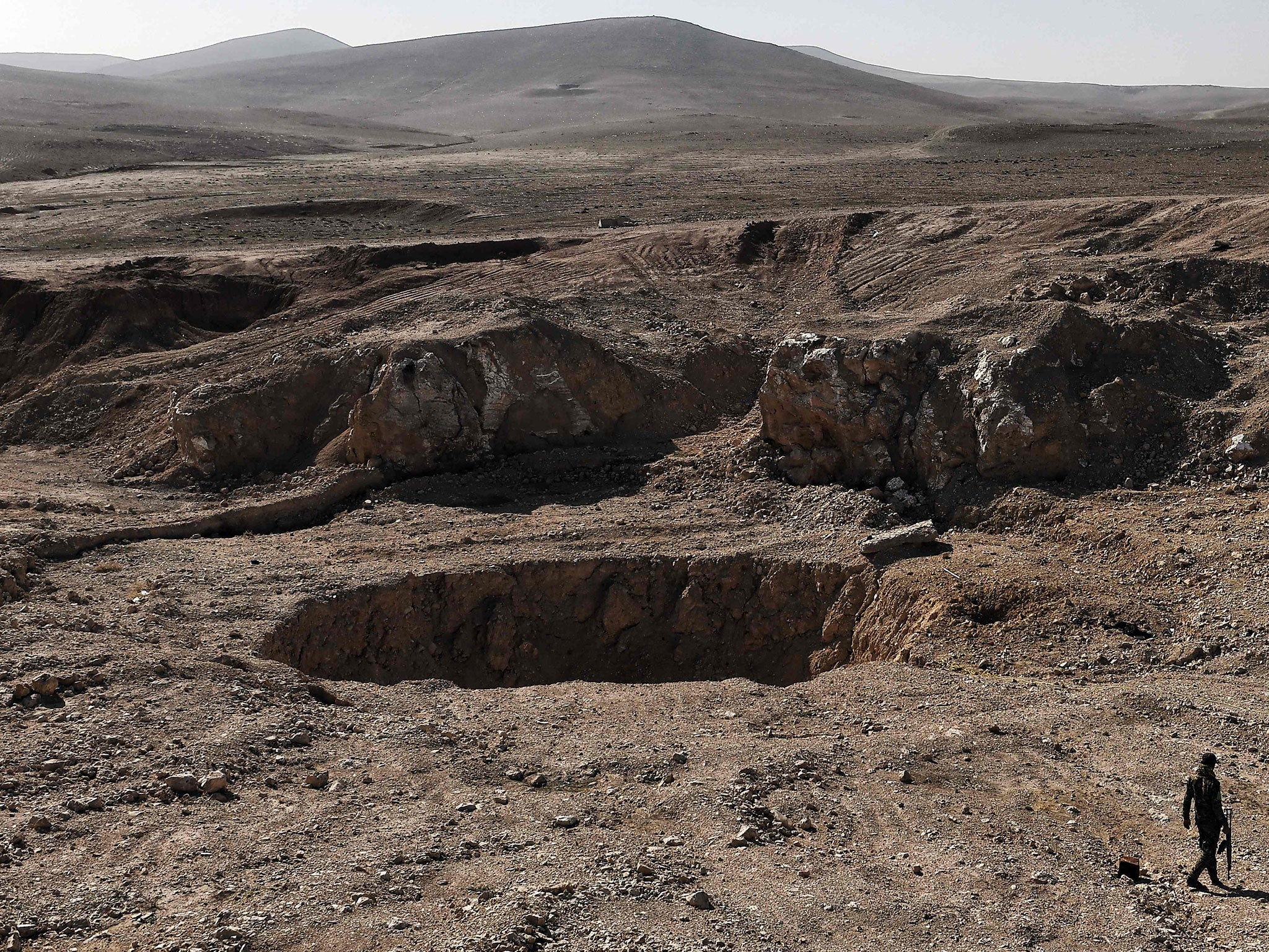 A member of the Popular Mobilisation Forces walks next to the khasfah sinkhole and mass grave south of Mosul on 26 February