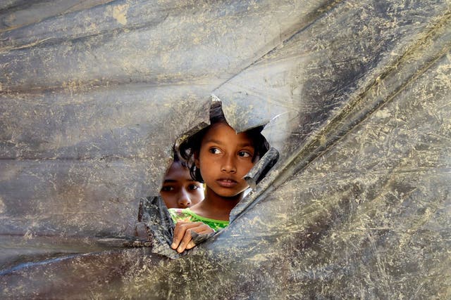 A Rohingya refugee girl peeks through a hole made in a plastic wall dividing the shelters at Balu Kali Refugee Camp in Cox's Bazar, Bangladesh, 28 February, 2017