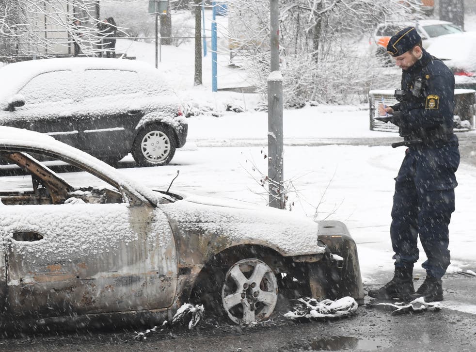 A police man investigate a burned out car in the suburb Rinkeby outside Stockholm.