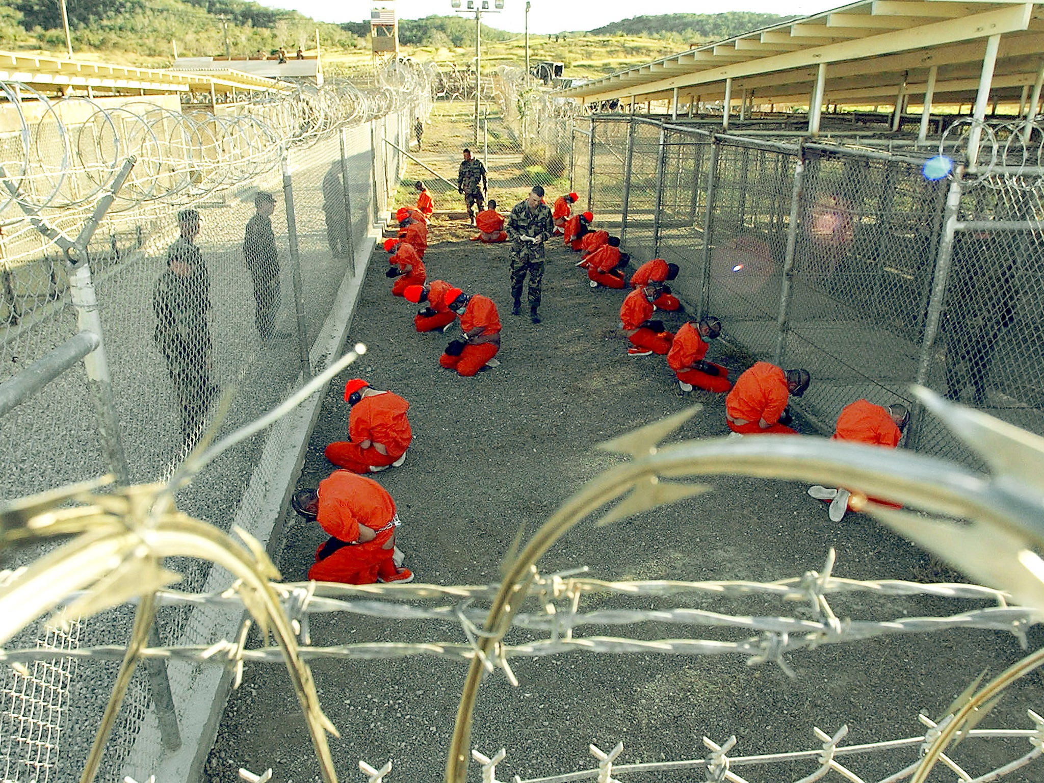 US Navy, US Military Police guard Taliban and al Qaeda detainees in orange jumpsuits in a holding area at Camp X-Ray at Naval Base Guantanamo Bay, Cuba