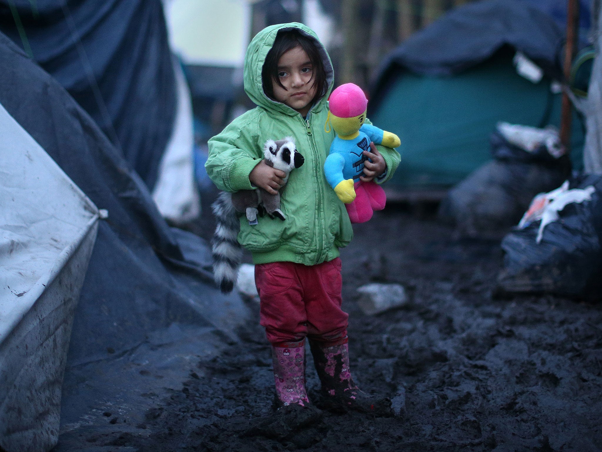 A young Kurdish girl holds her toys as she stands in the mud in a migrant camp in Dunkirk, France
