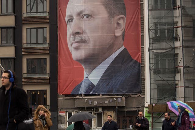 People walk past a large banner showing the portrait of Turkish President Recep Tayyip Erdogan in Taksim Square