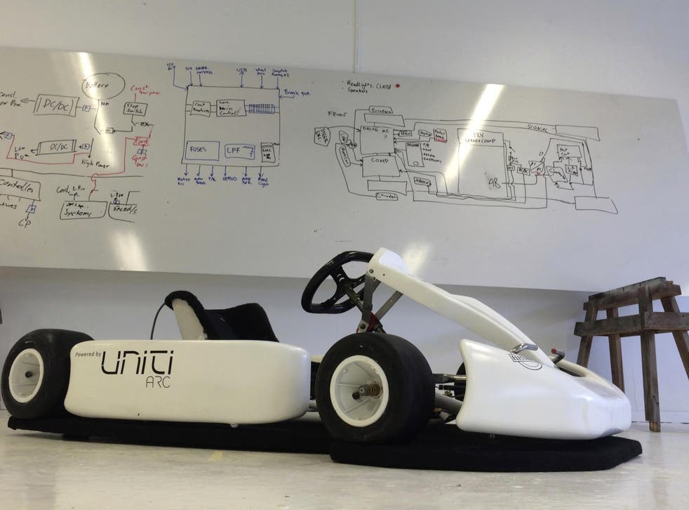 A Uniti-branded go kart sits in front a white board filled with engineering sketches in the start-up's temporary production facility in Lund
