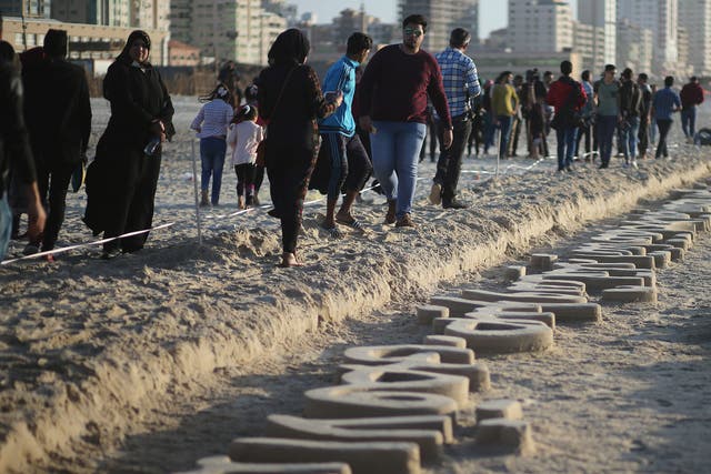 Palestinians walk near sand sculptures depicting Palestinian heritage, made by local artist Osama Sbeata, on a beach in Gaza City