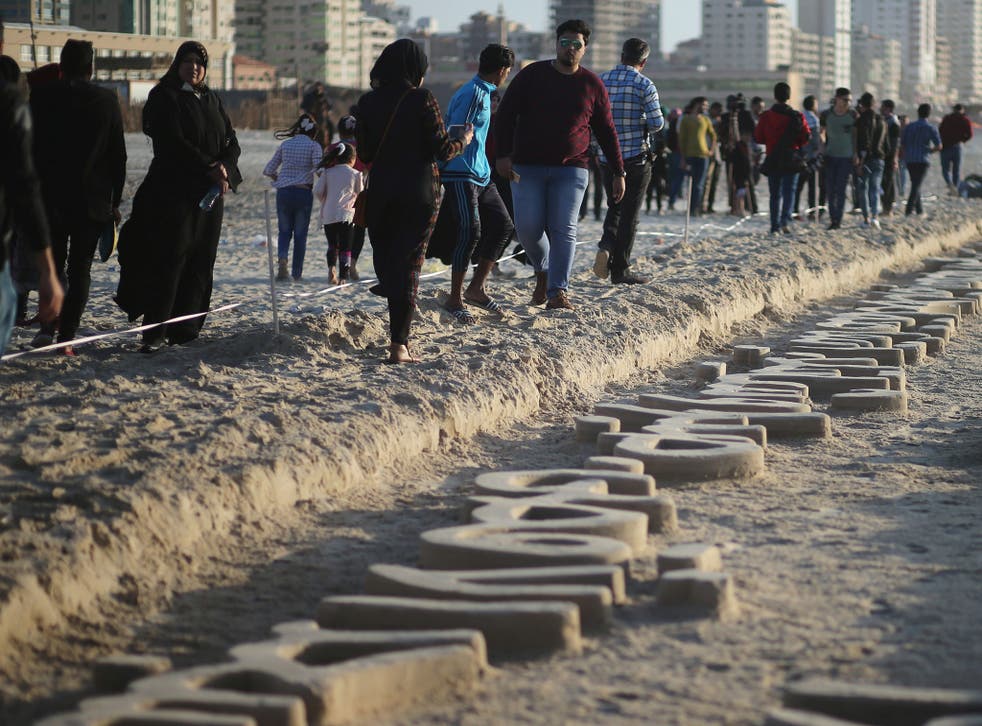 Palestinians walk near sand sculptures depicting Palestinian heritage, made by local artist Osama Sbeata, on a beach in Gaza City