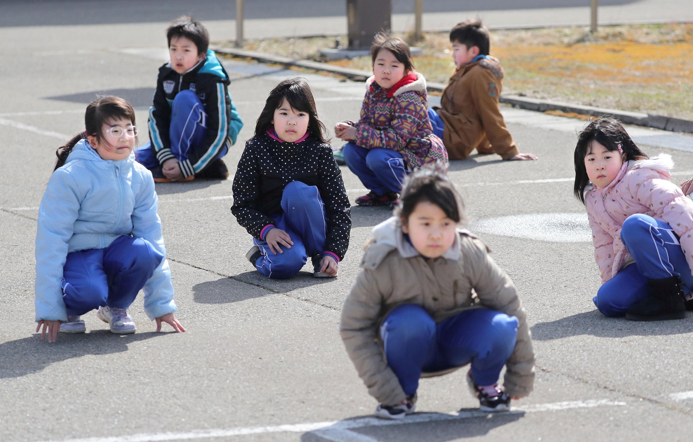 Pupils squat down on the street as they participate in an evacuation drill in the Japanese city of Oga