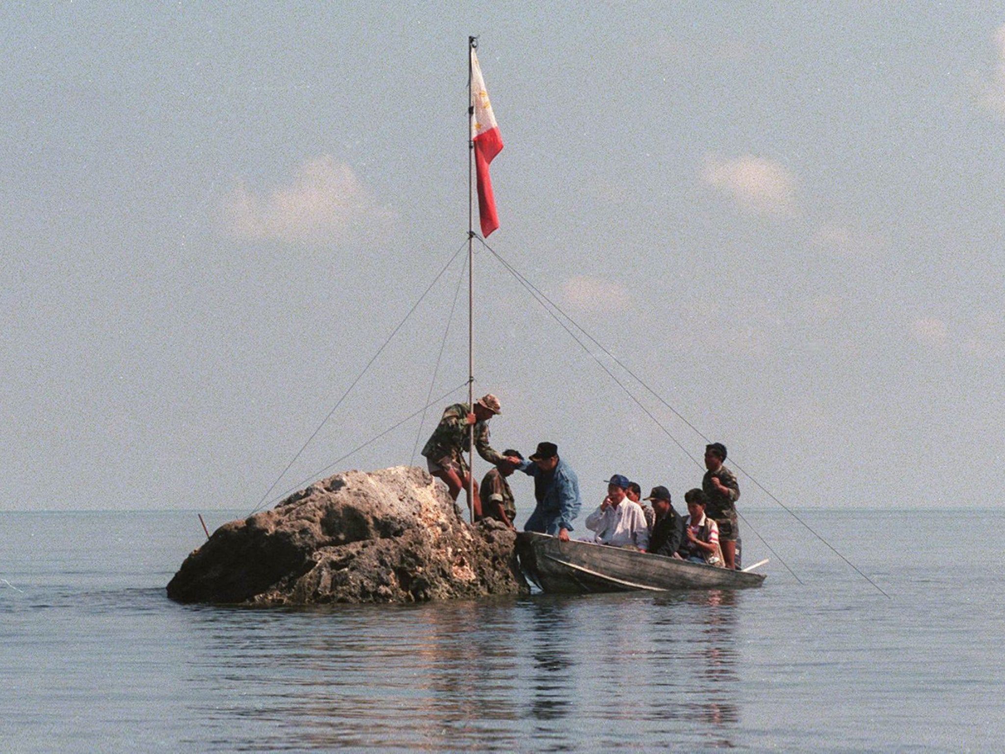 A team of navy personnel and three Philippine congressmen standing on a tiny rock in the Scarborough Shoal with a Filipino flag in protest at Chinese land grabbing
