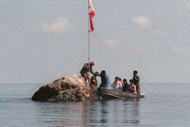 A team of navy personnel and three Philippine congressmen standing on a tiny rock in the Scarborough Shoal with a Filipino flag in protest at Chinese land grabbing
