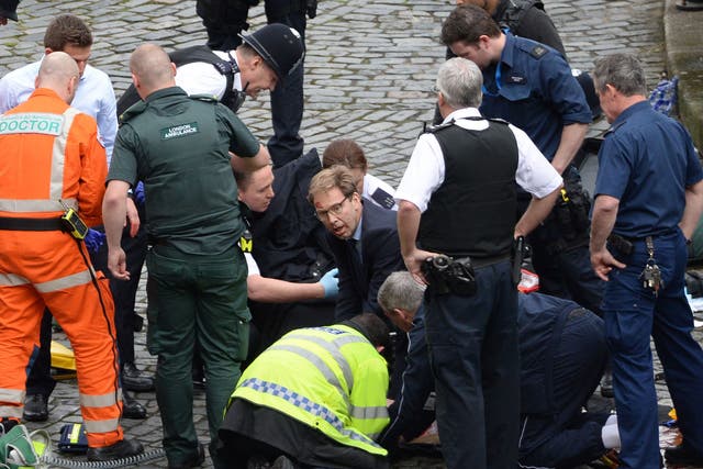 Conservative MP Tobias Ellwood (centre) helps emergency services attend to a police officer outside the Palace of Westminster