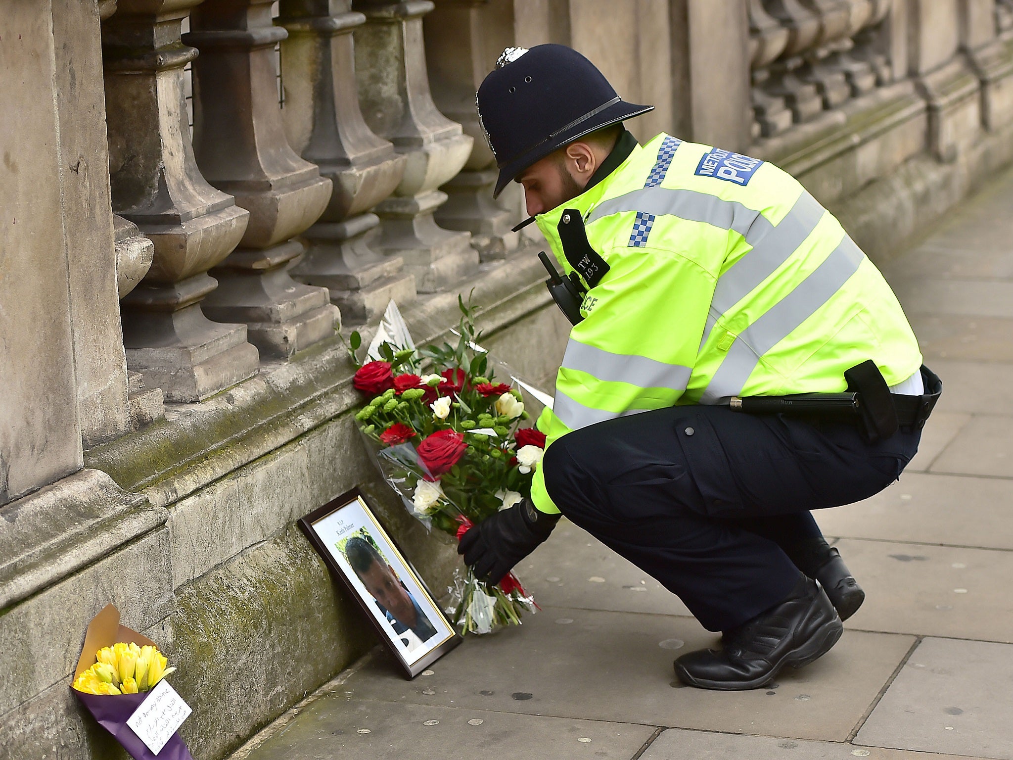 A police officer places flowers and a photo of PC Keith Palmer on Whitehall near the Houses of Parliament