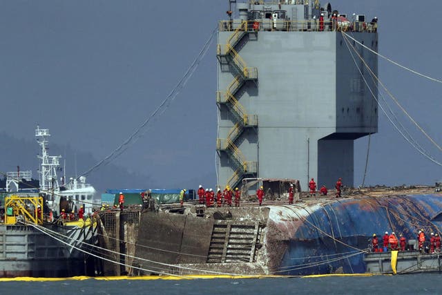 Workers try to raise the sunken Sewol ferry between two barges during the salvage operation in waters off Jindo, South Korea