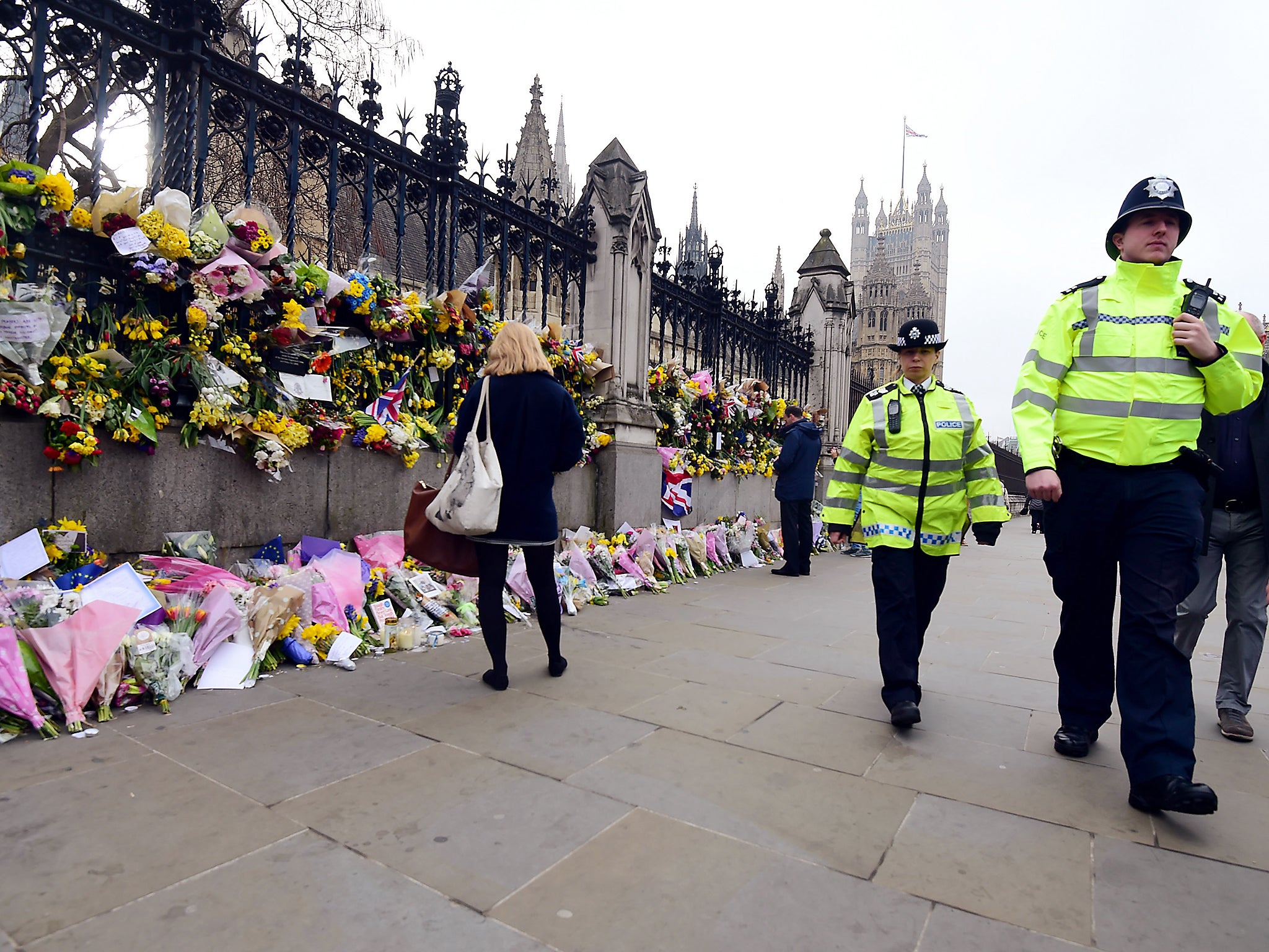 Police walk past floral tributes to the victims of the Westminster terrorist attack outside the Palace of Westminster, London (PA)