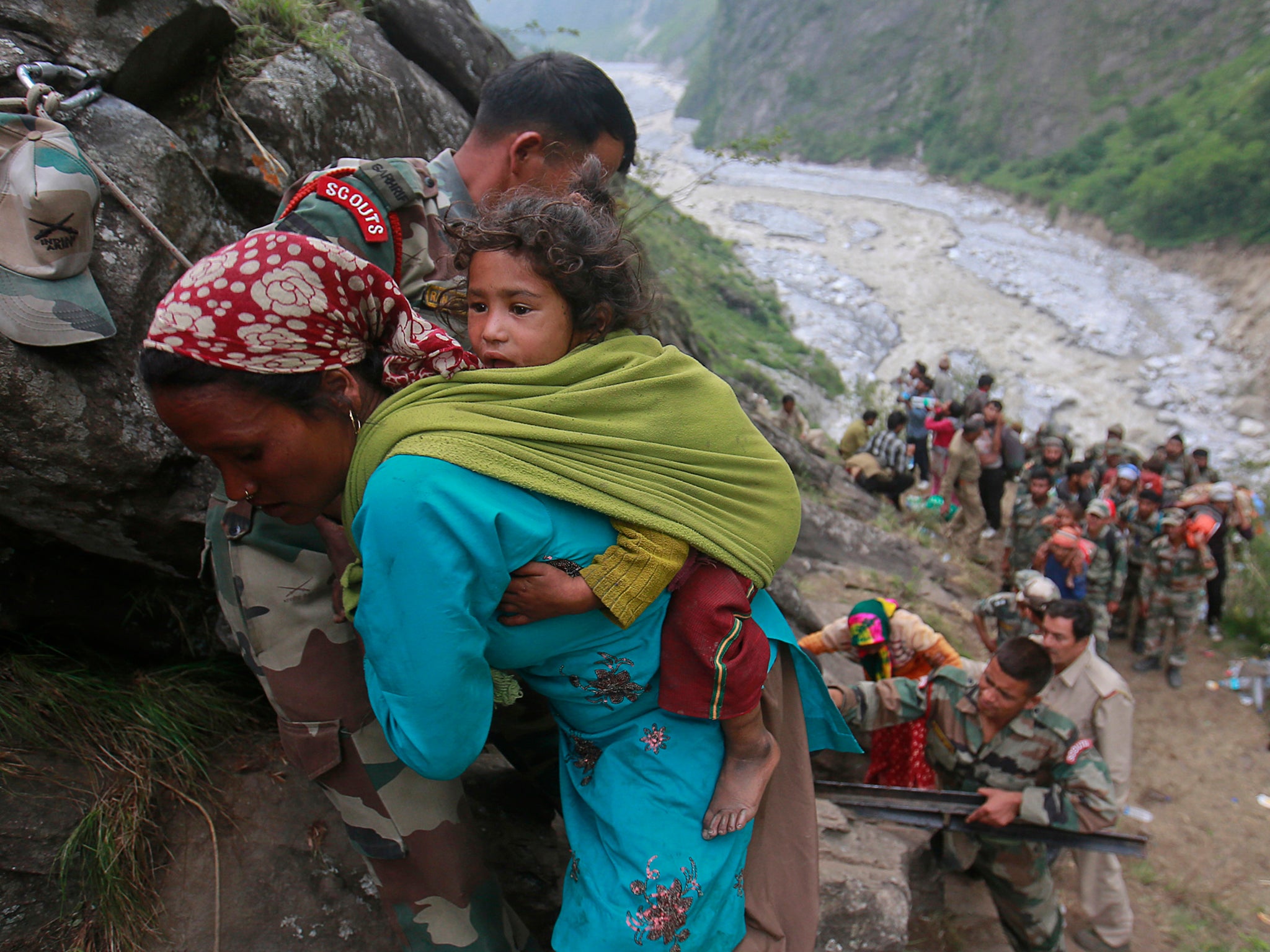 Soldiers assist a woman carrying a child on her back during rescue operations in Govindghat in the Himalayan state of Uttarakhand during the 2013 floods