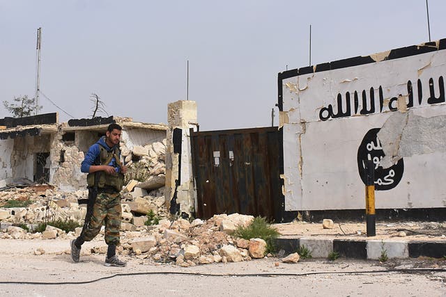  A member of the Syrian government forces walks past Isis graffiti in Syria