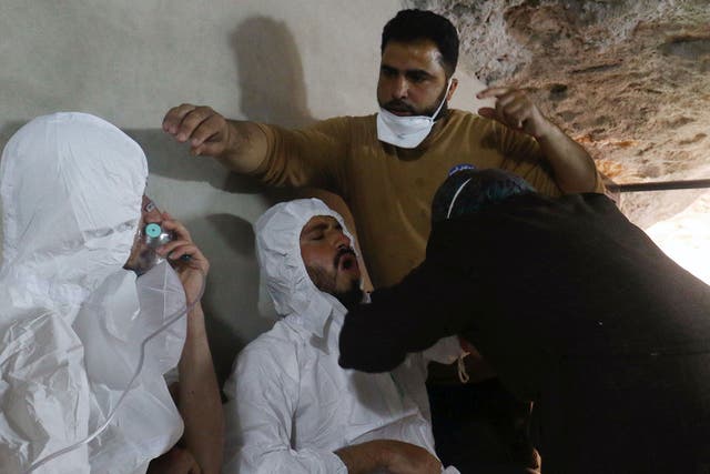 A man breathes through an oxygen mask as another one receives treatment, after what rescue workers described as a suspected gas attack in the town of Khan Sheikhoun on Tuesday