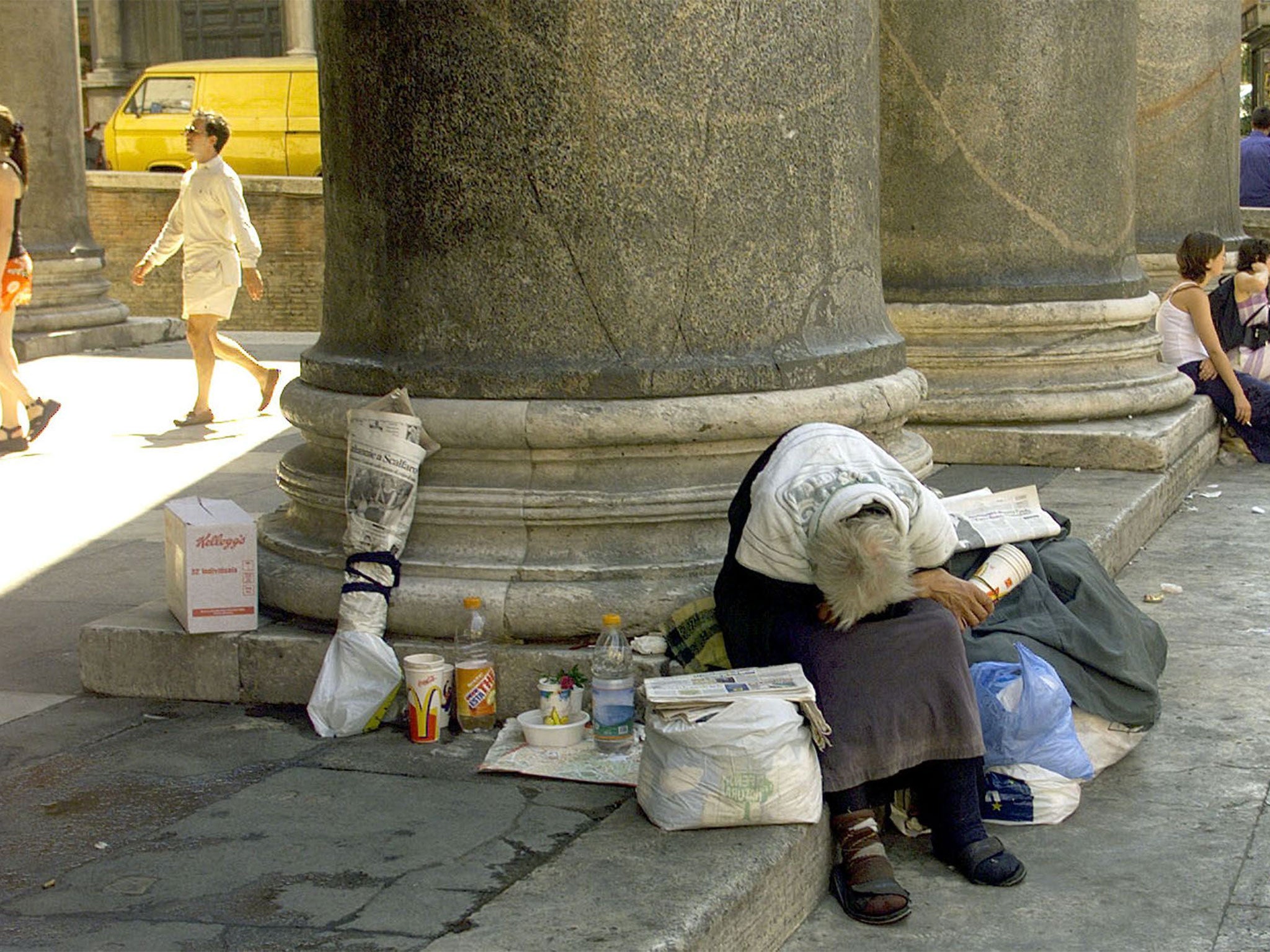 An elderly homeless person rests in the shadow of the Pantheon, central Rome