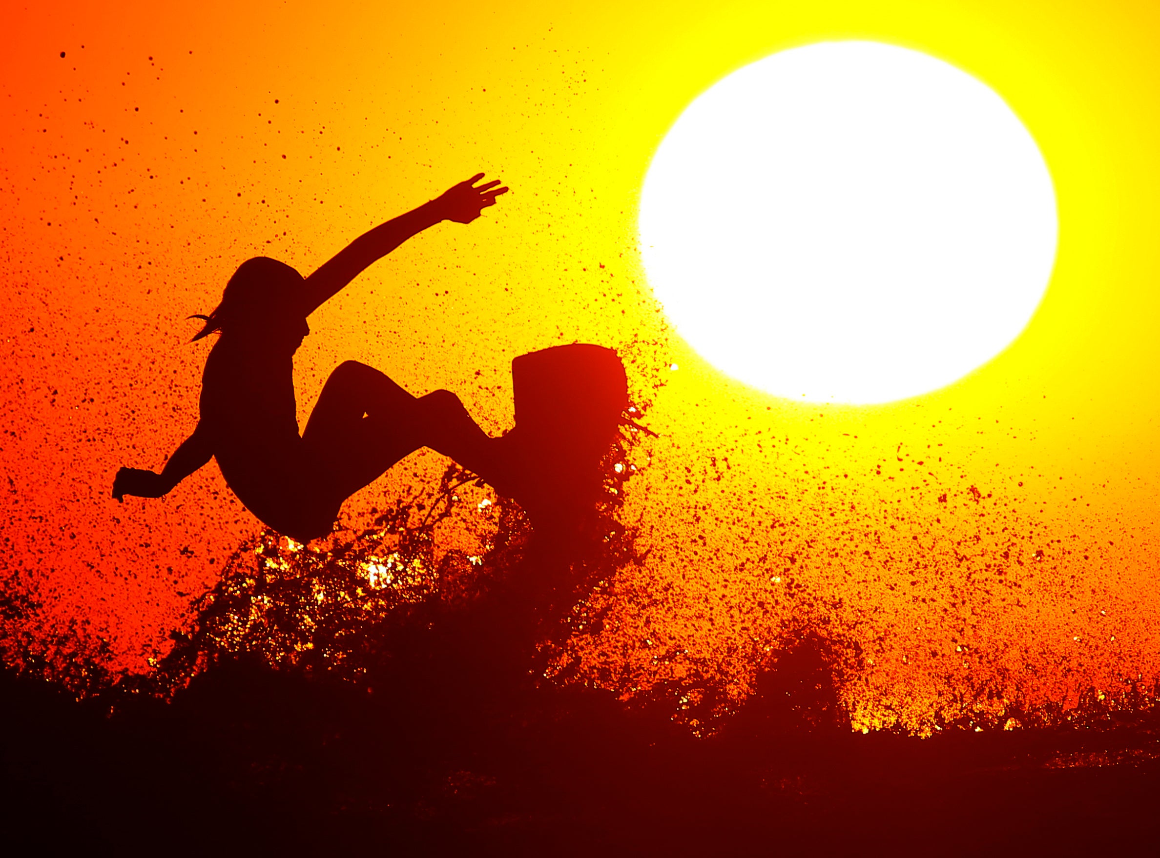 Surfer Cole Clisby rides his surfboard off the top of a wave as the sun sets off the shores of Leucadia, California