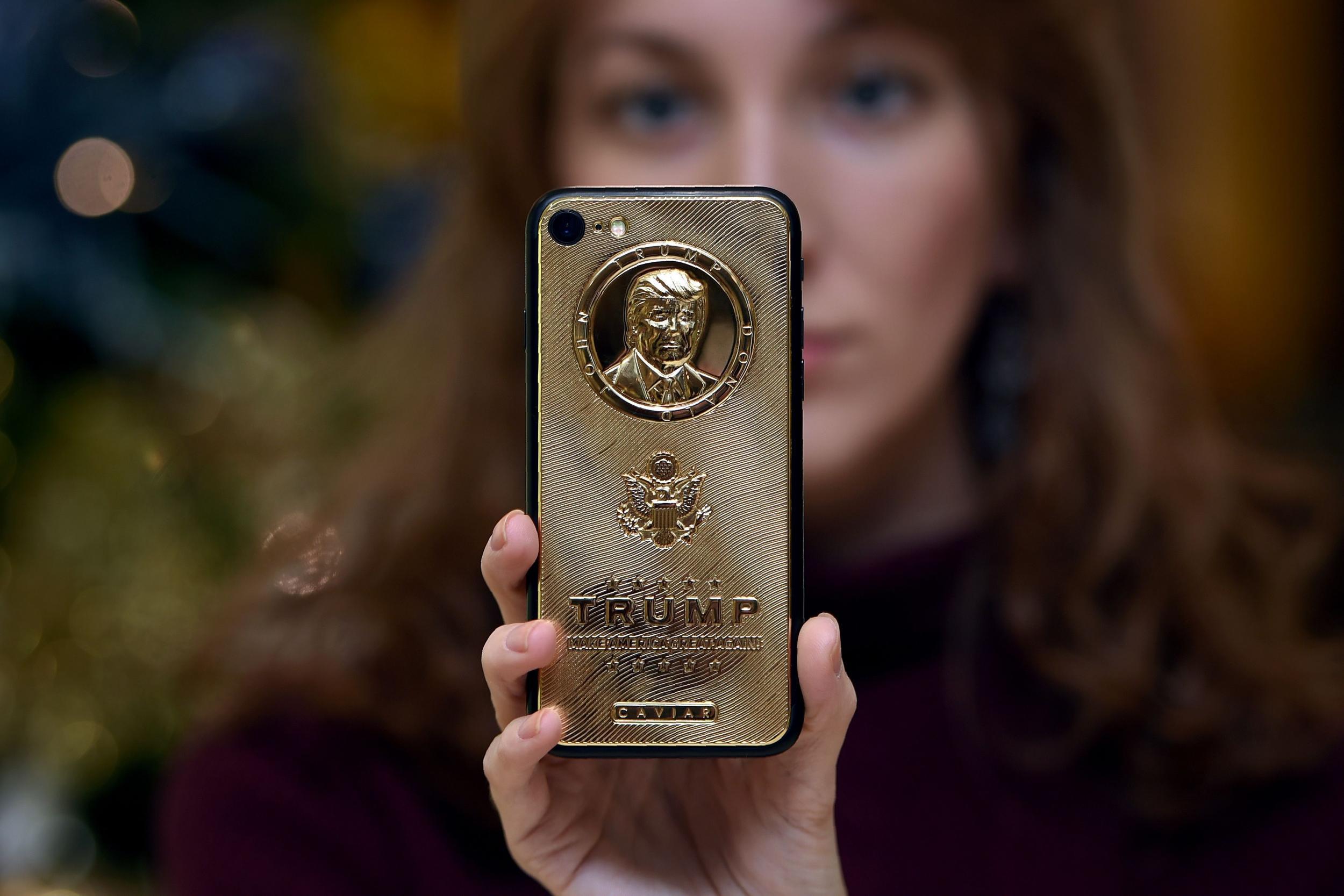 An employee of Caviar Phones displays a gold-plated iPhone case emblazoned with President Donald Trump's image