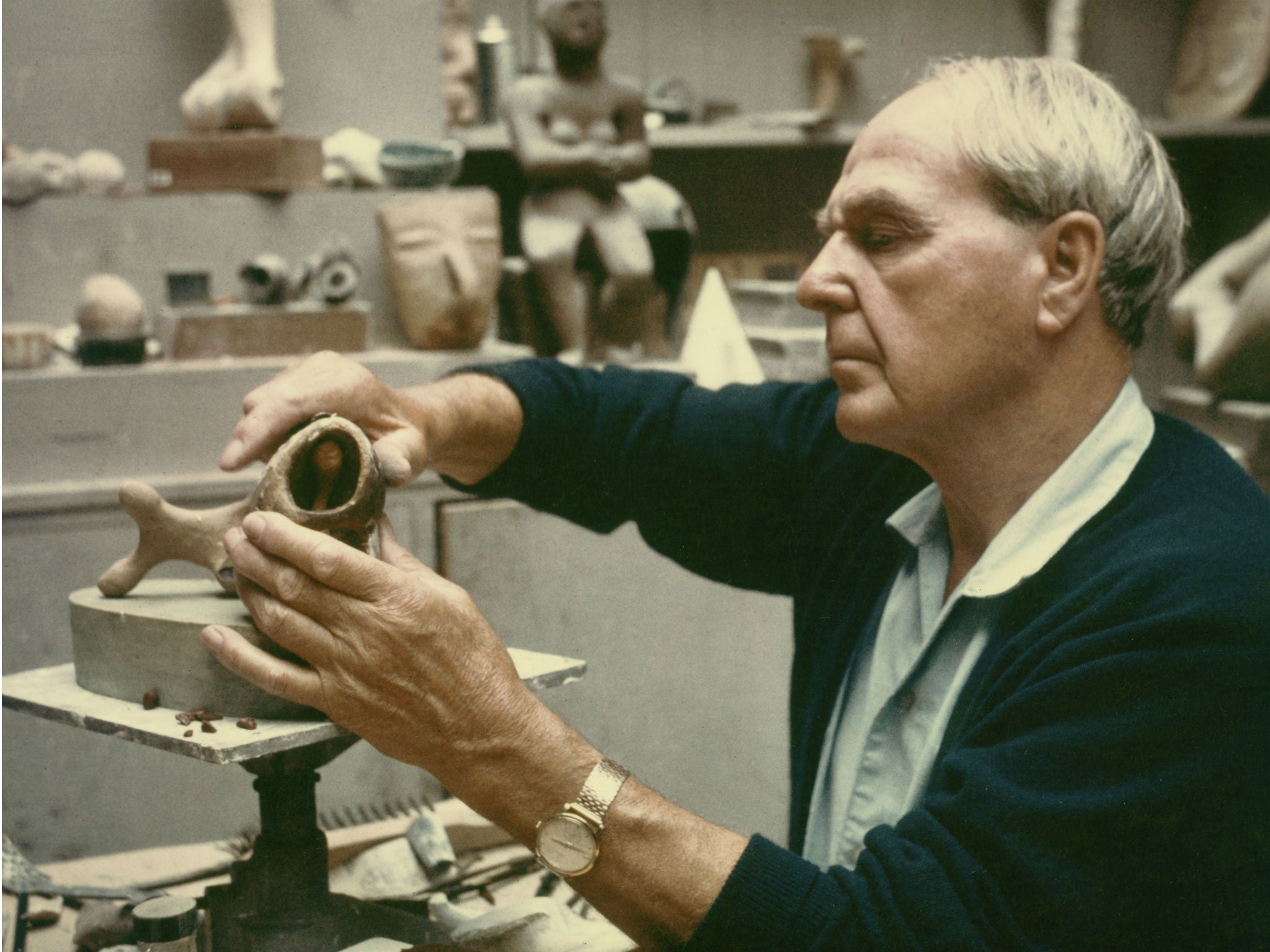 Henry Moore working on a plaster maquette in his studio c.1968 with Seated Figure 1929 cast concrete (LH 65) and an Aztec head clearly visible on the shelf behind