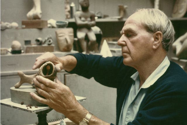 Henry Moore working on a plaster maquette in his studio c.1968 with Seated Figure 1929 cast concrete (LH 65) and an Aztec head clearly visible on the shelf behind