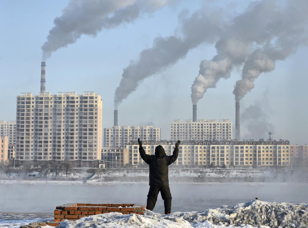 An elderly man exercises on the banks of the Songhua River in Jilin, China, as smoke billows from huge chimneys
