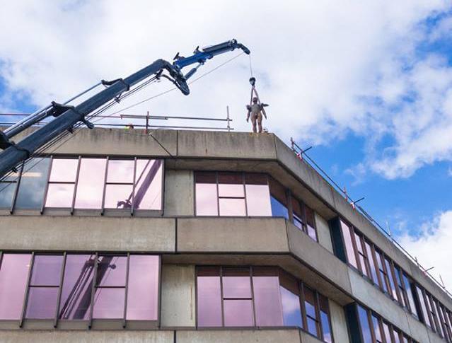 An Antony Gormley sculpture from the series 'Another Place' is lifted onto a roof at UEA