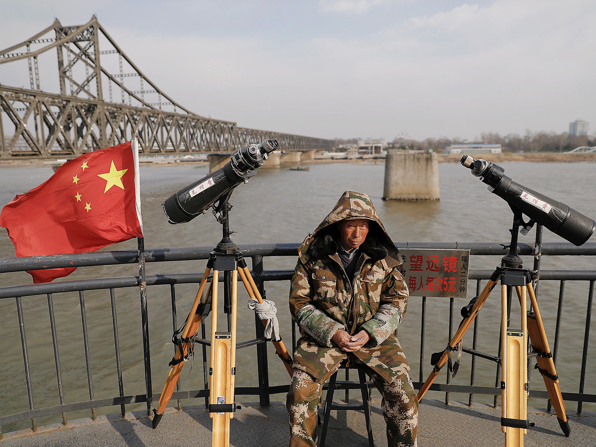 File: A man sits between binoculars he offers to tourists to watch the North Korean side of the Yalu River from the Broken Bridge, bombed by the US forces in the Korean War and now a tourist site, in Dandong, China's Liaoning province. The bridge connects China’s Dandong New Zone to North Korea’s Sinuiju