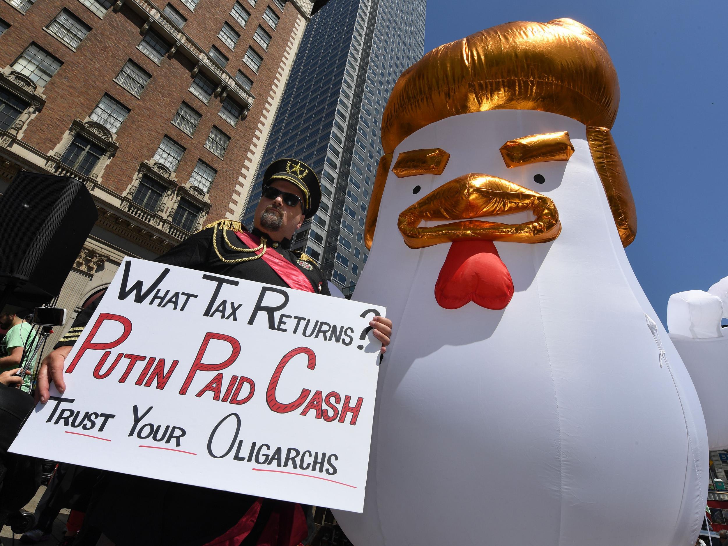 Mike Stutz dressed as a Russian general stands beside a giant Trump chicken as he joins protesters taking part in the 'Tax March' in Los Angeles, California (Getty)