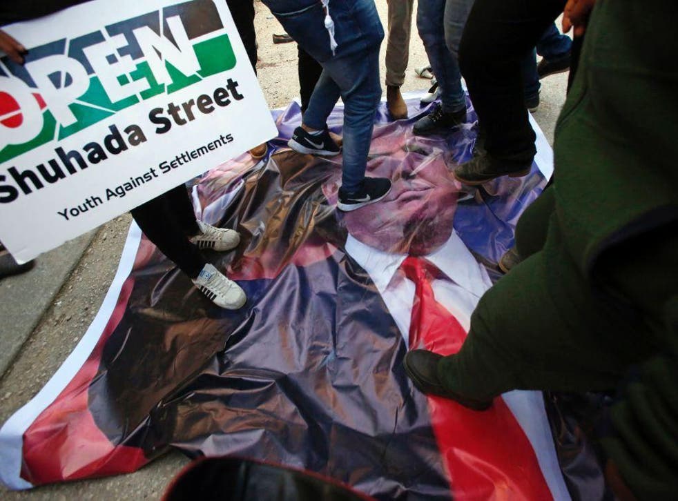 Palestinian demonstrators stand on a poster of US President Donald Trump as they protest against his support of Israel and demand for the Israeli army to re-open Shuhada Street near a Jewish settlement in Hebron on 24 February, 2017