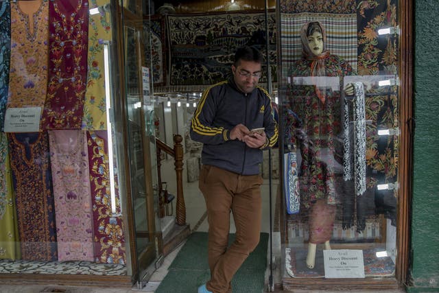 A Kashmiri shopkeeper browses the internet on his mobile phone