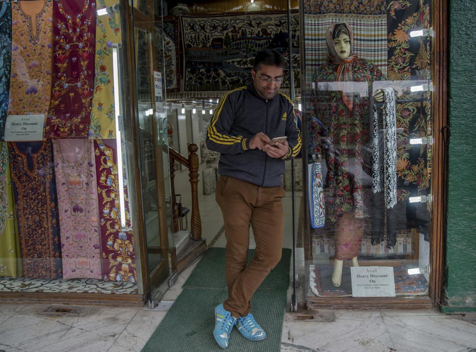 A Kashmiri shopkeeper browses the internet on his mobile phone