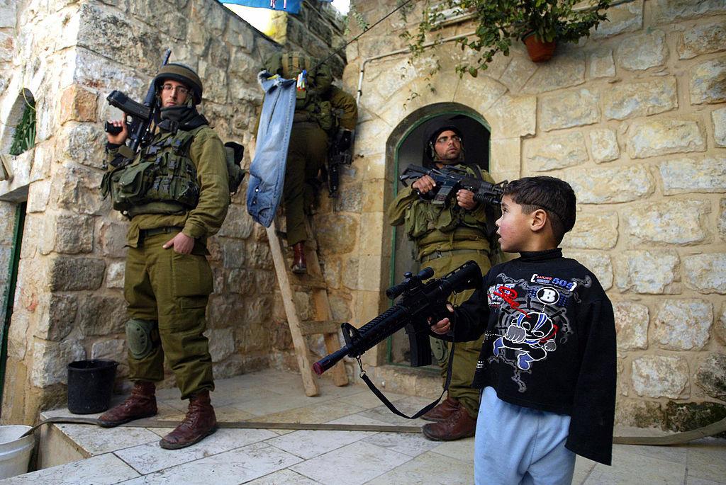 A Palestinian boy plays with his plastic rifle as Israeli soldiers search homes and rooftops in the West Bank town of Hebron in this file photo from 29 December 2006