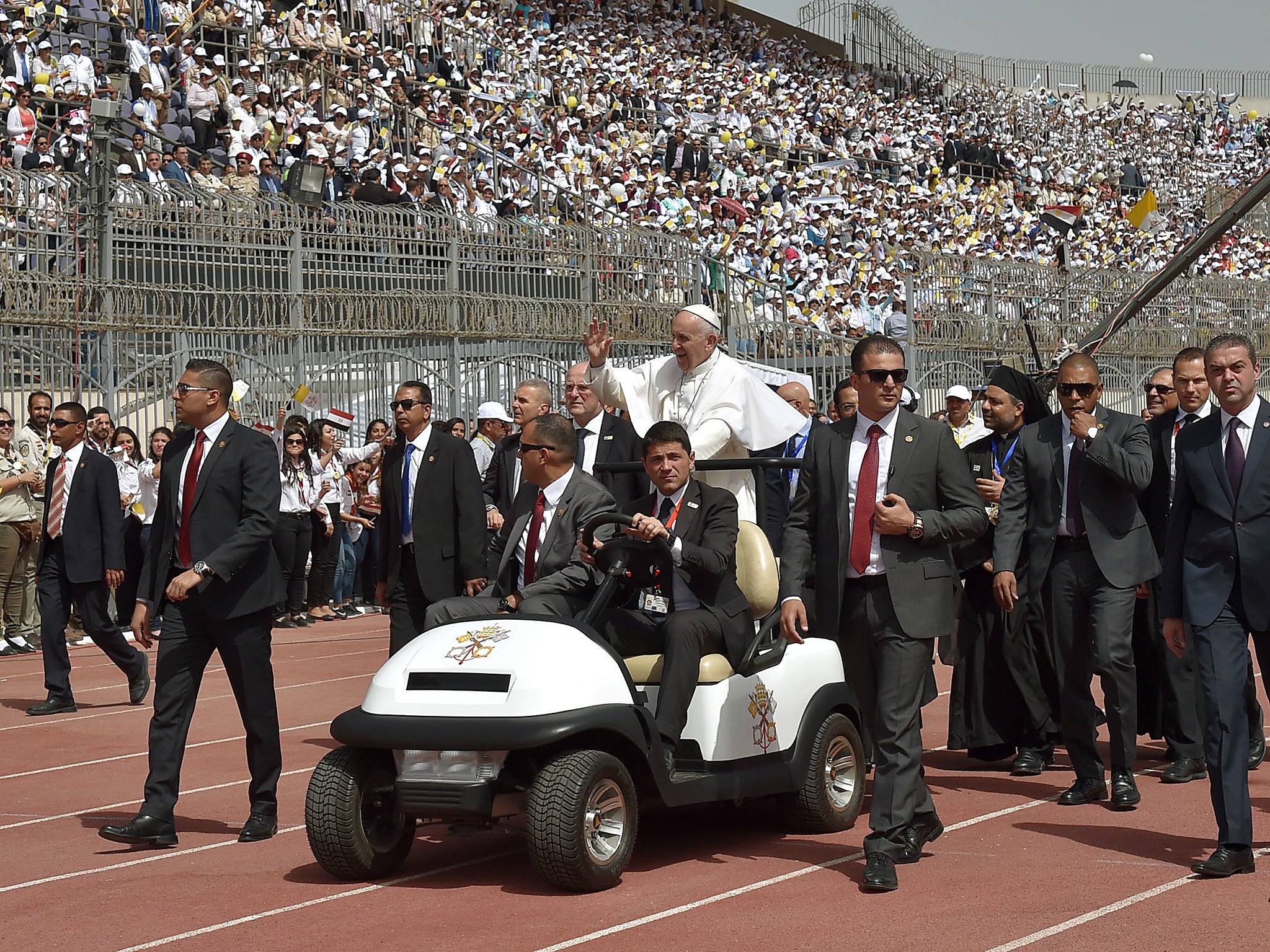 Pope Francis is surrounded by security as he rides an uncovered Popemobile before the start of a mass at a stadium in Cairo