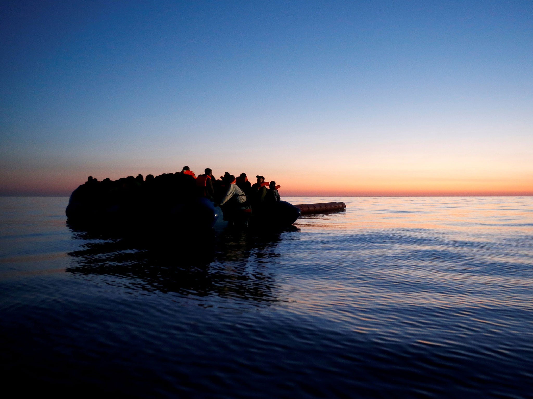 Refugees on a rubber dinghy await rescue at dawn in the central Mediterranean