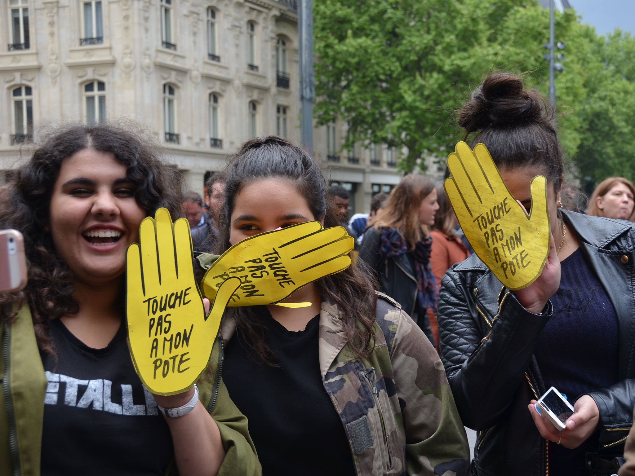 French students at the anti-racism rally hold up yellow hand-shaped cards reading 'Don't harm my friend'