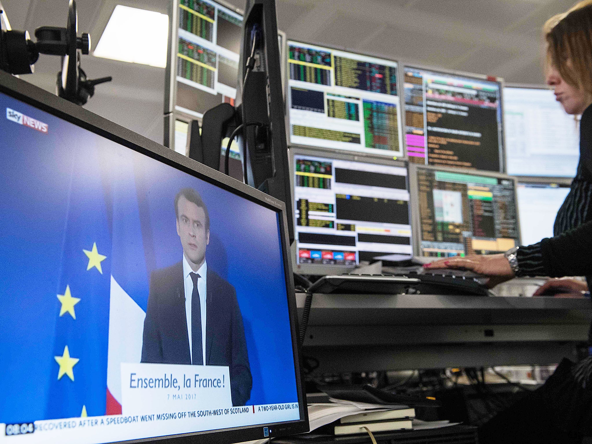 A television screen displays an image of France's President-elect Emmanuel Macron, as traders works on the trading floor of ETX Capital in London