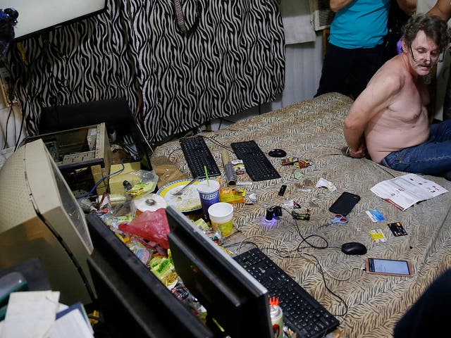David Timothy Deakin, from Peoria, Ill., with his hands tied behind his back during a raid by investigators, sits on his bed where he handles online sharing of videos of children engaging in sexual acts in Mabalacat, Philippines