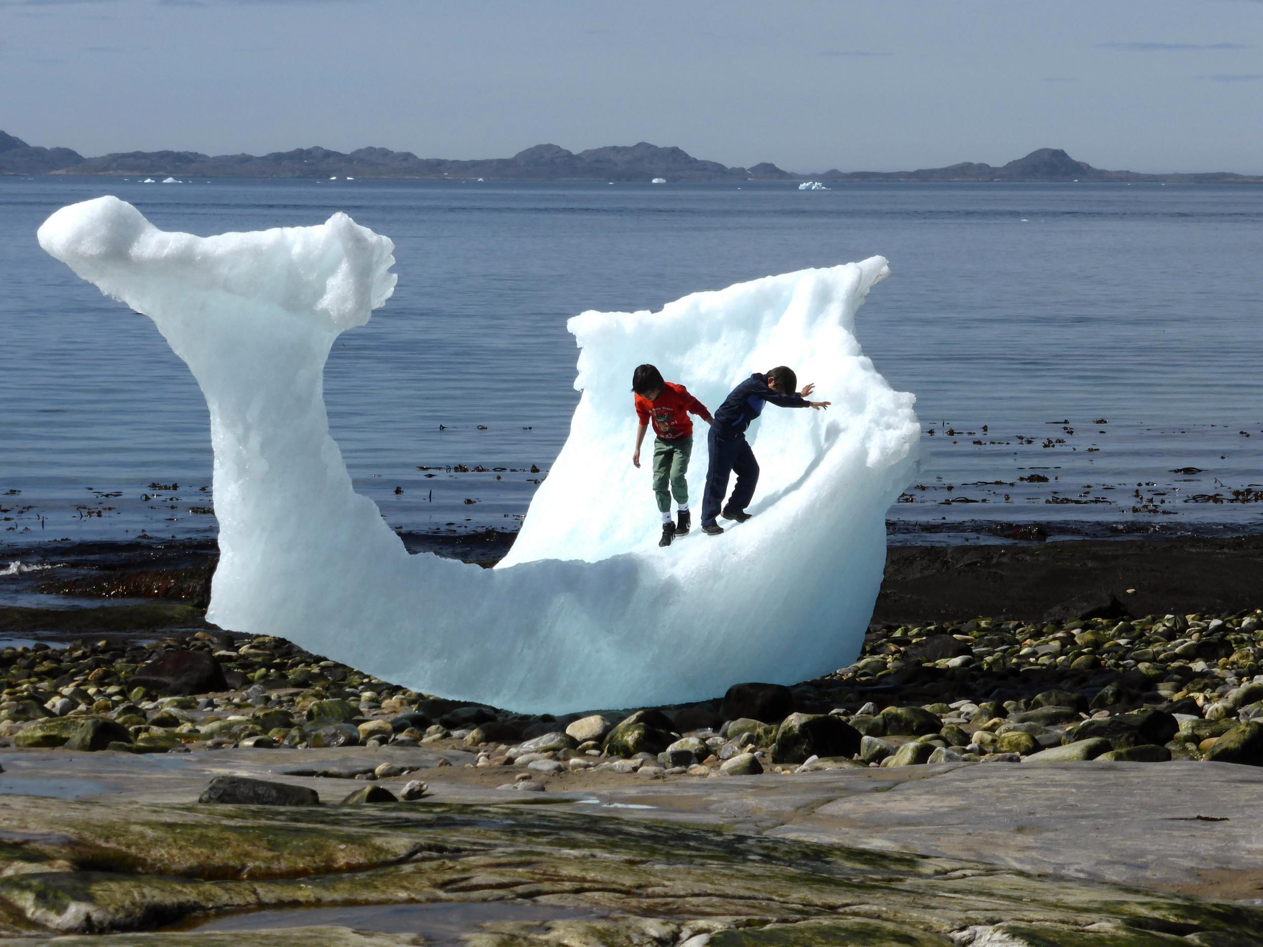 Children play on the remains of a stranded iceberg on a beach in Nuuk, Greenland