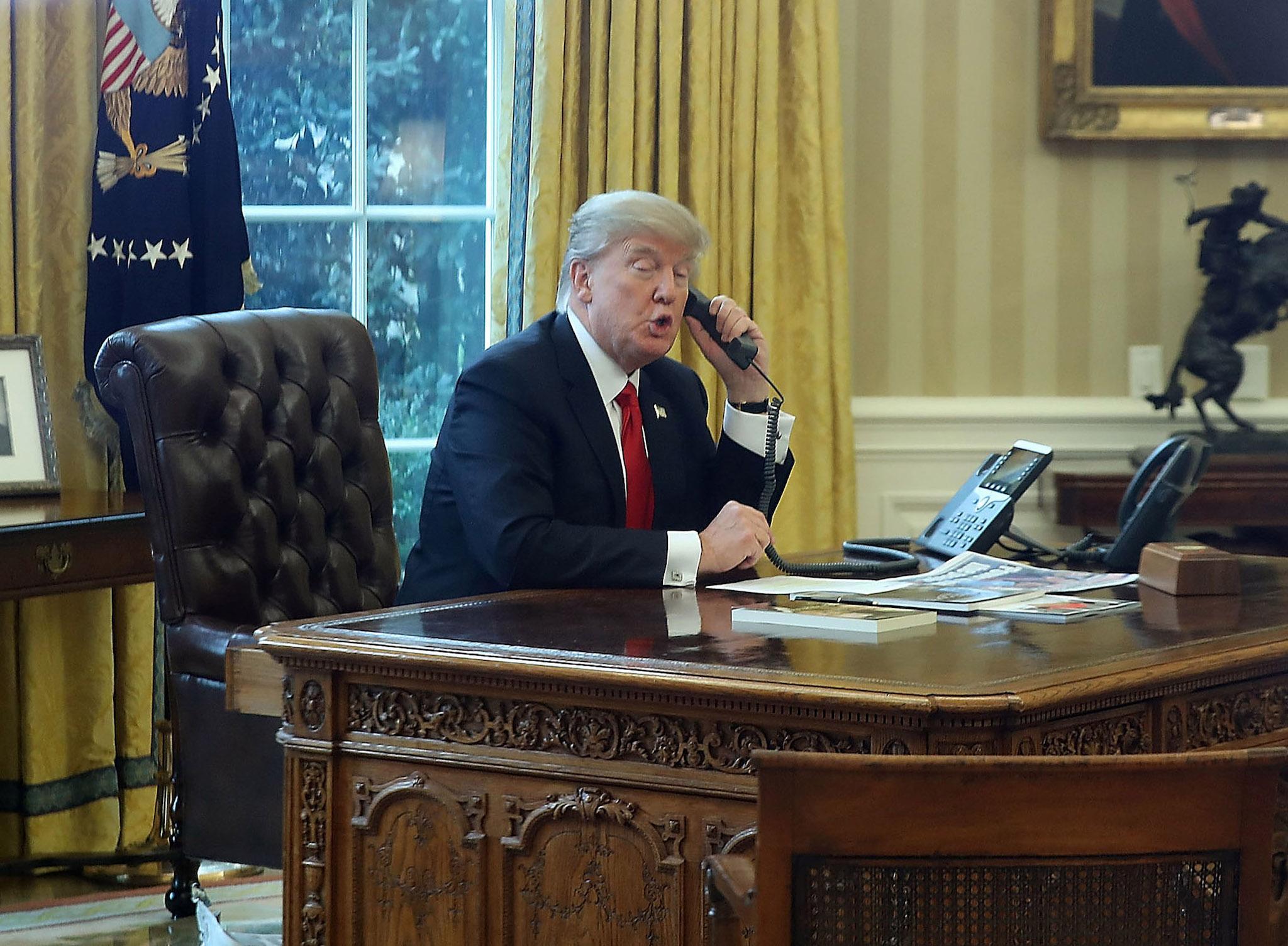 President Donald Trump is seen through a window speaking on the phone with King of Saudi Arabia, Salman bin Abd al-Aziz Al Saud, in the Oval Office of the White House