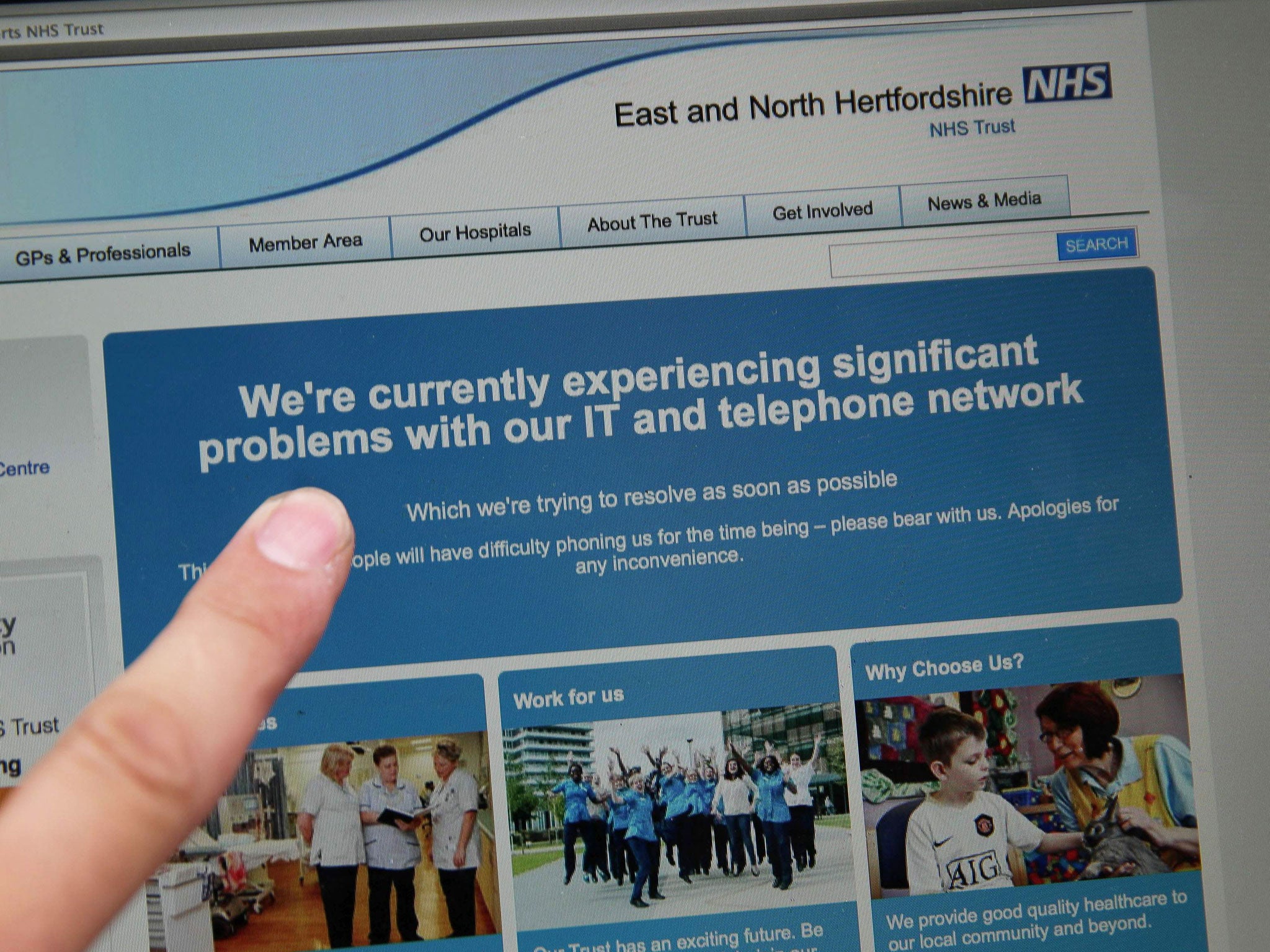 A woman points to the website of the NHS: East and North Hertfordshire notifying users of a problem in its network