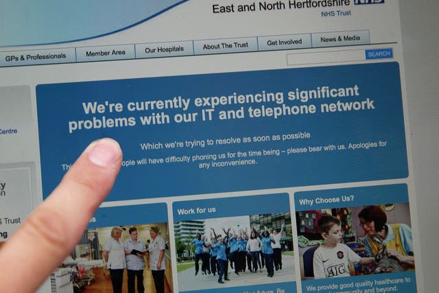 A woman points to the website of the NHS: East and North Hertfordshire notifying users of a problem in its network