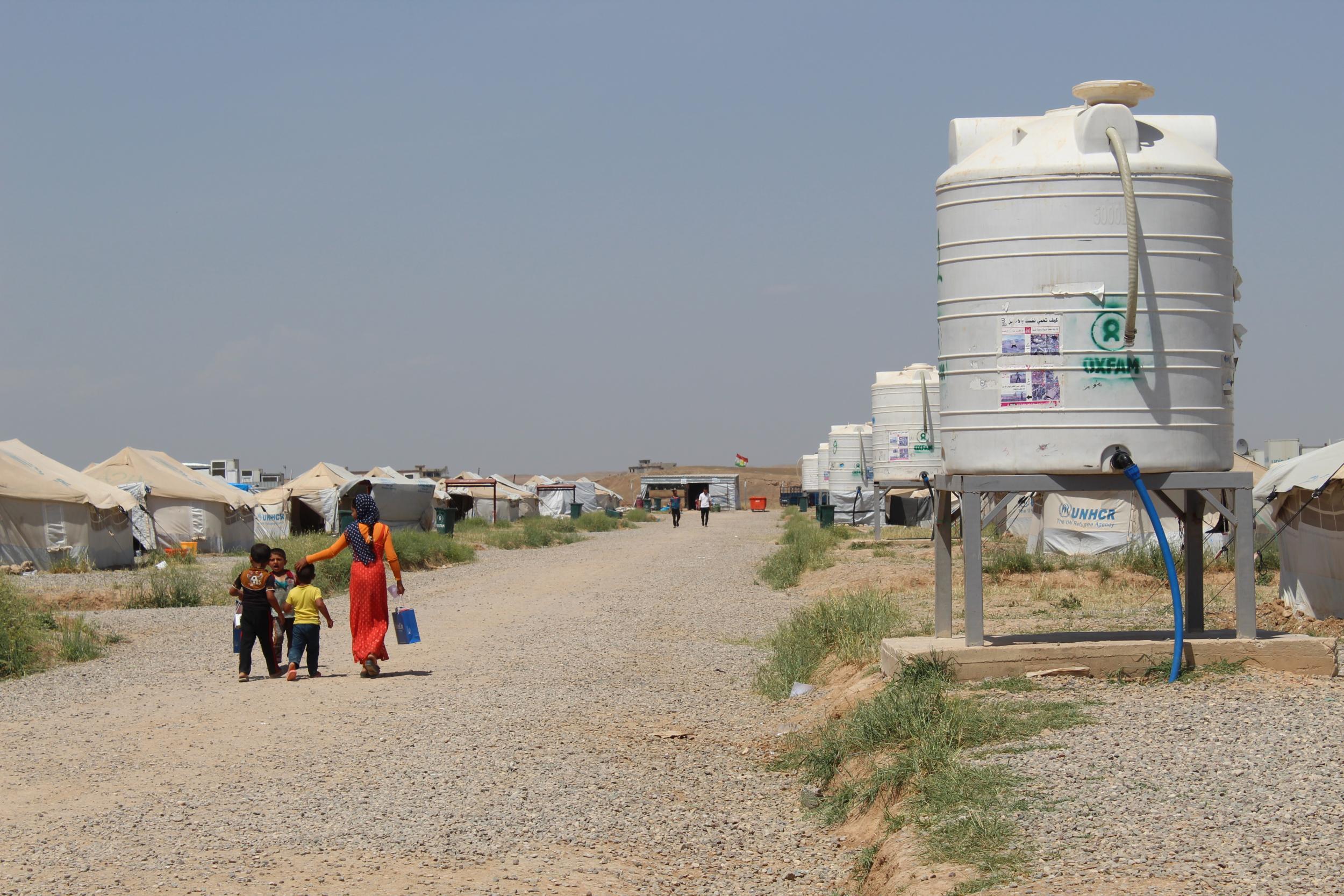 A family walks past a drinking water tank at Hasensham IDP camp, 30 km (18 miles) to the east of Mosul