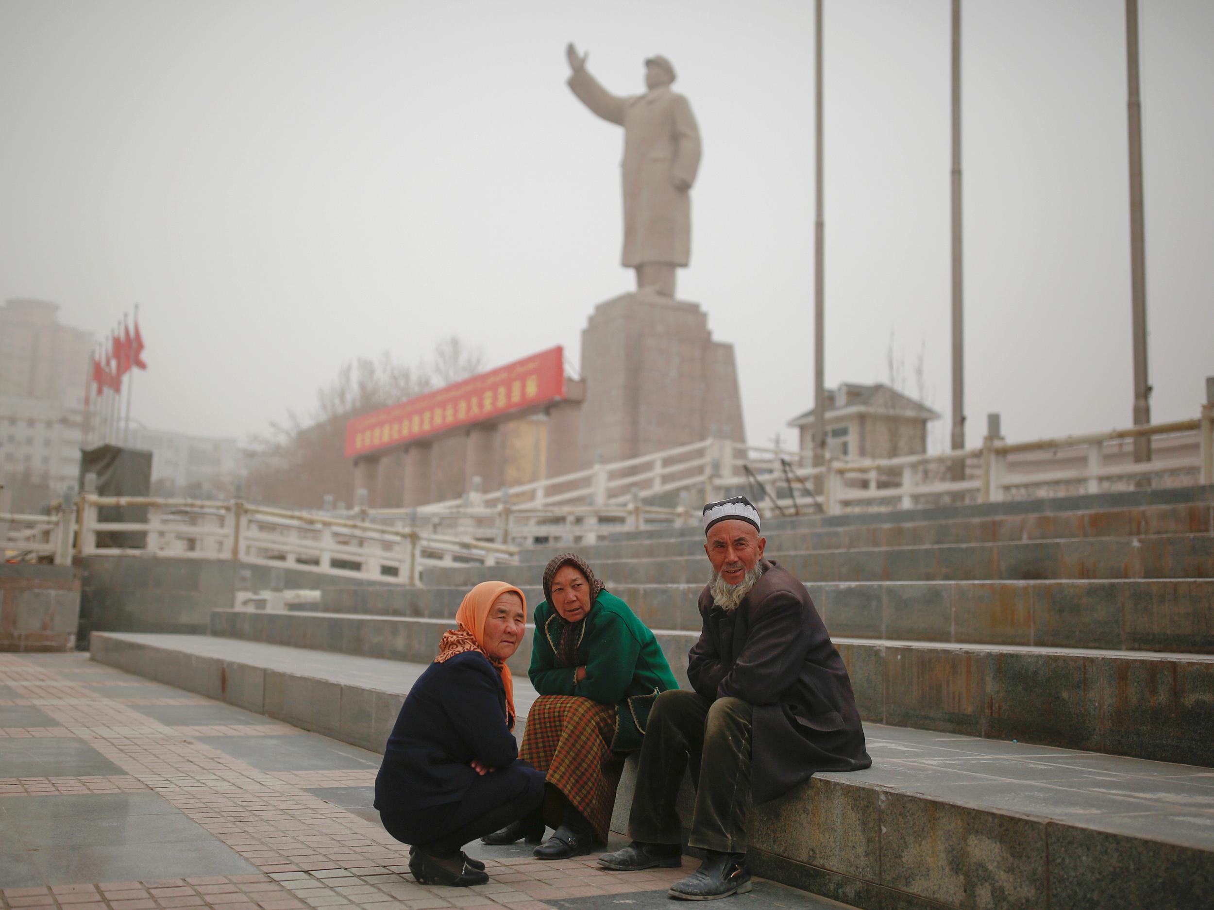 Ethnic Uighurs sit near a statue of China's late Chairman Mao Zedong in Kashgar, Xinjiang
