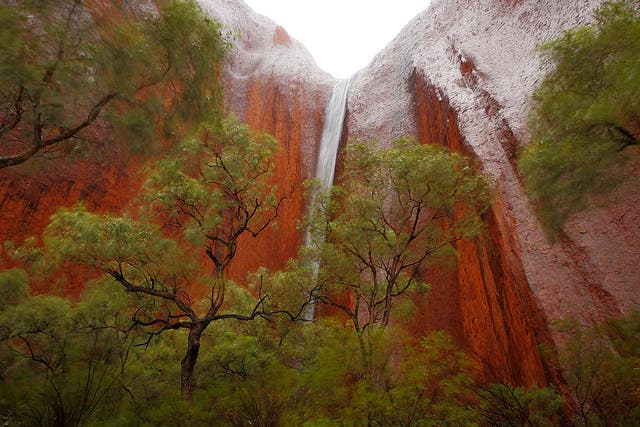 The torrential rains cause waterfalls to cascade down Uluru